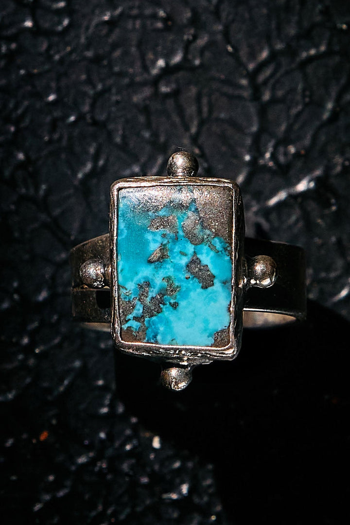 Silver ring with a rectangular turquoise stone on a textured black background