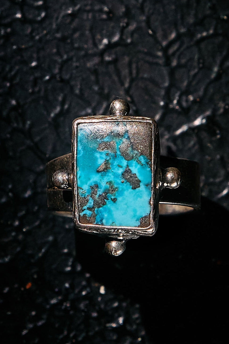 Silver ring with a rectangular turquoise stone on a textured black background