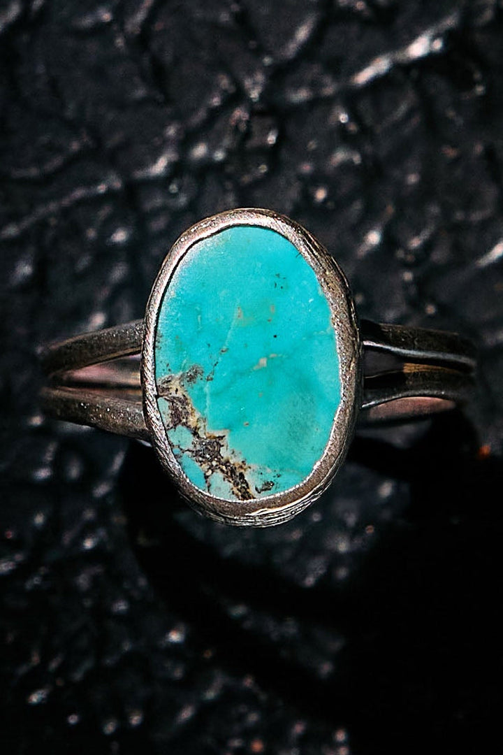 Turquoise ring with silver band on a textured black background