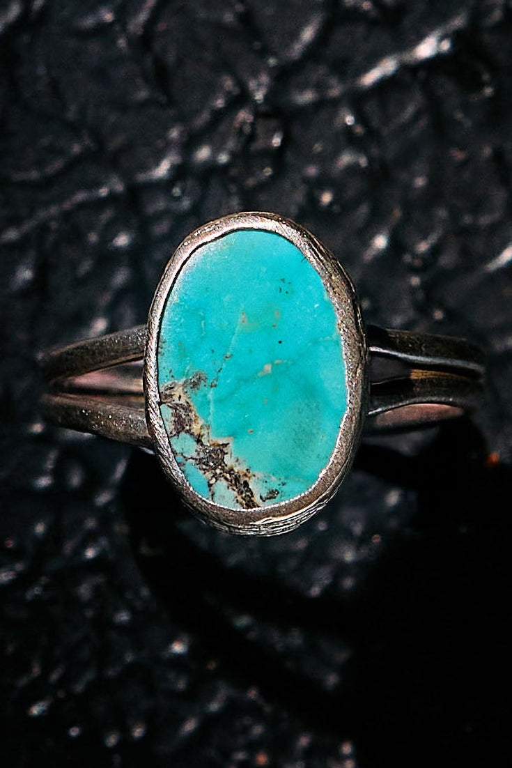 Turquoise ring with silver band on a textured black background