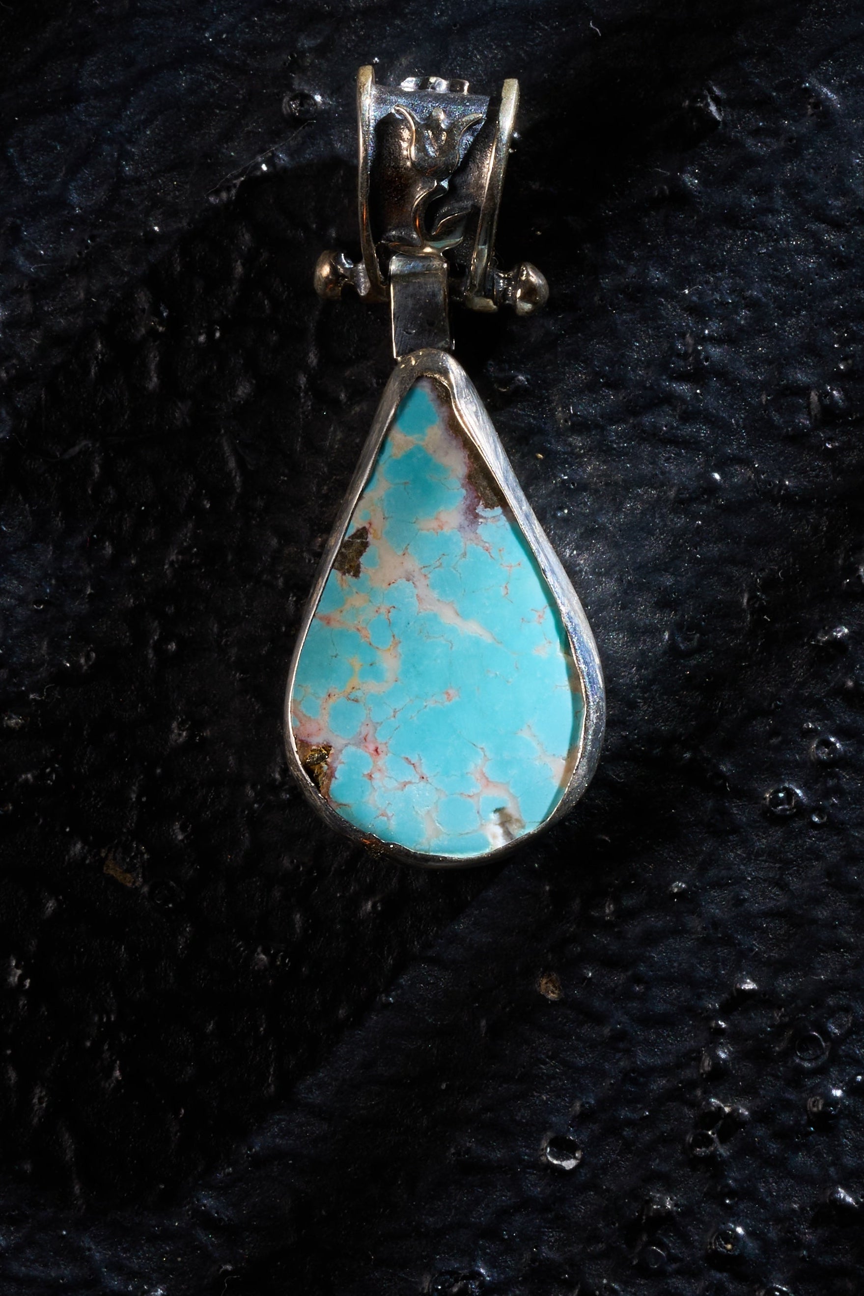 Turquoise pendant with silver setting on a textured black surface