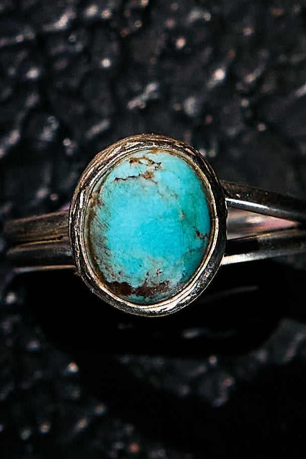 Turquoise ring with silver band on a dark textured background