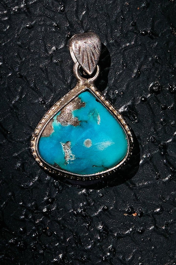 Turquoise pendant with silver setting on a black textured background