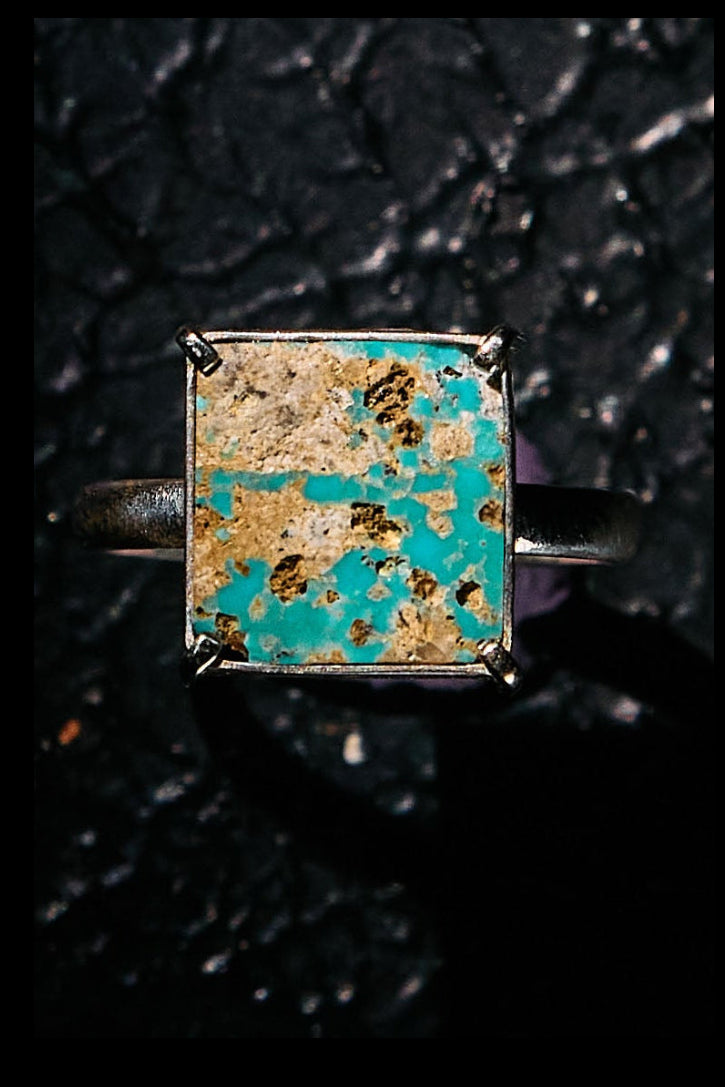 Ring with a square turquoise gemstone on a black textured background