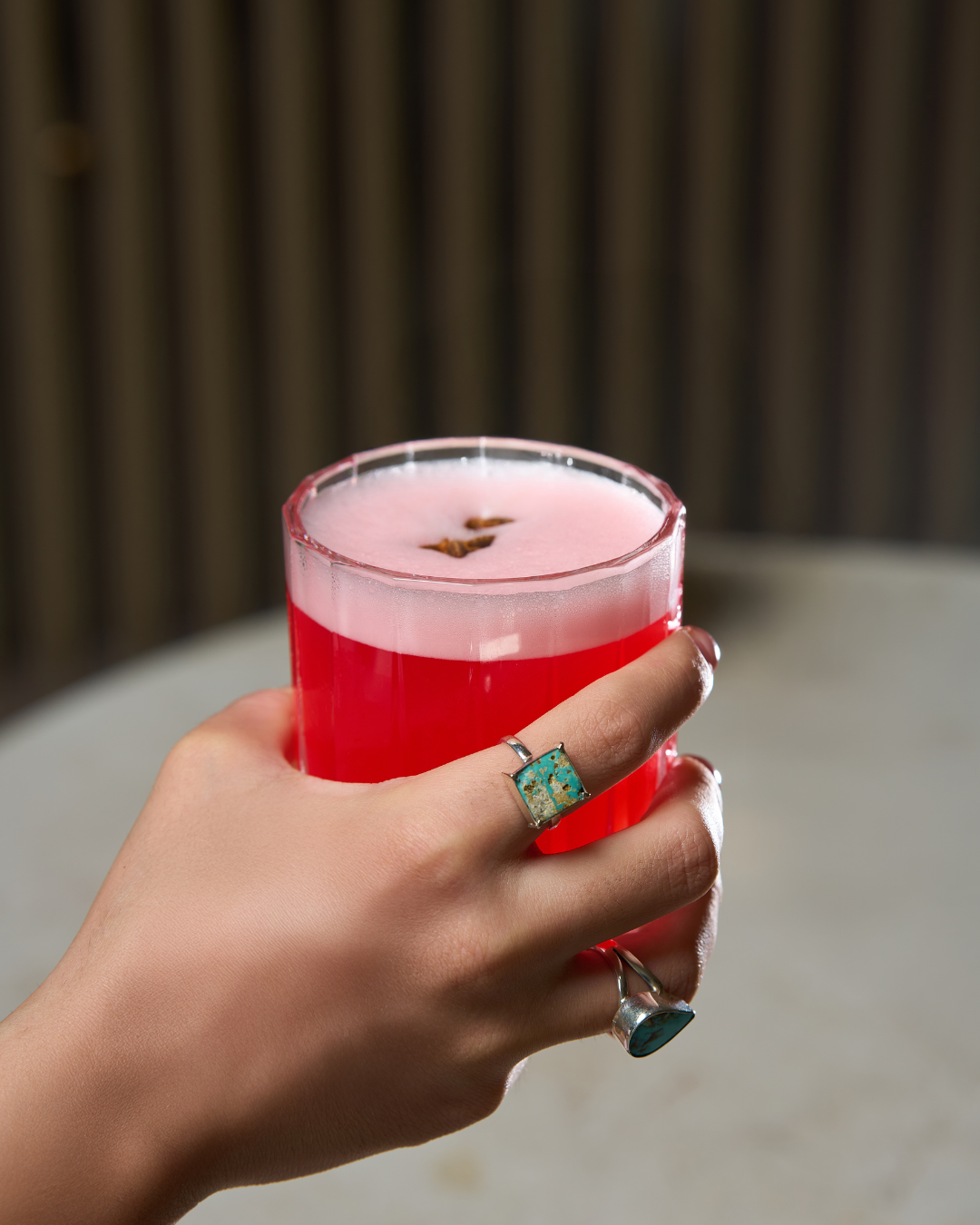 Hand holding a red cocktail with a turquoise ring on silver