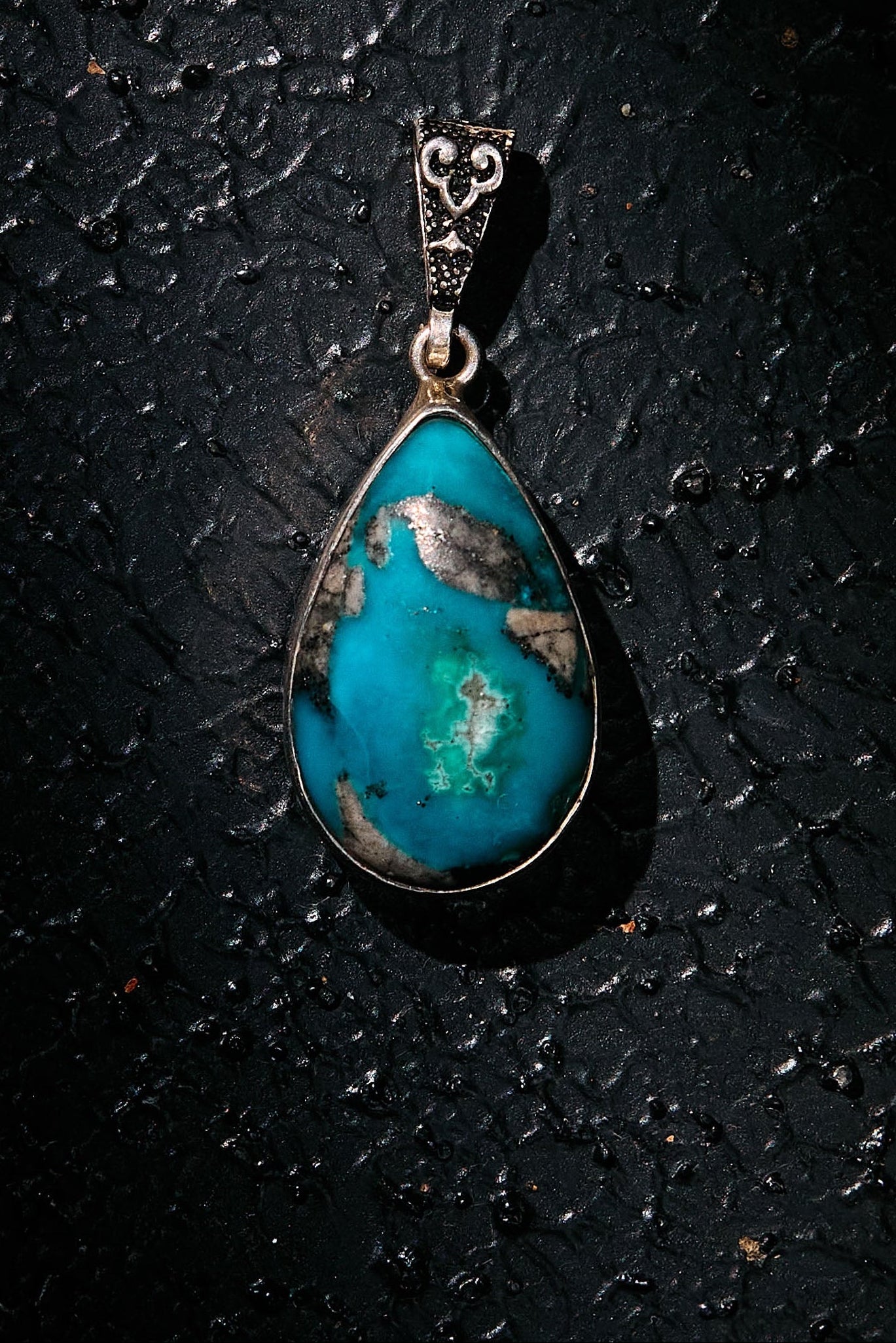 Teardrop-shaped turquoise pendant on a dark textured surface