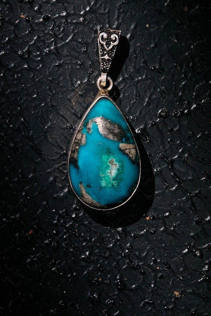 Teardrop-shaped turquoise pendant on a dark textured surface
