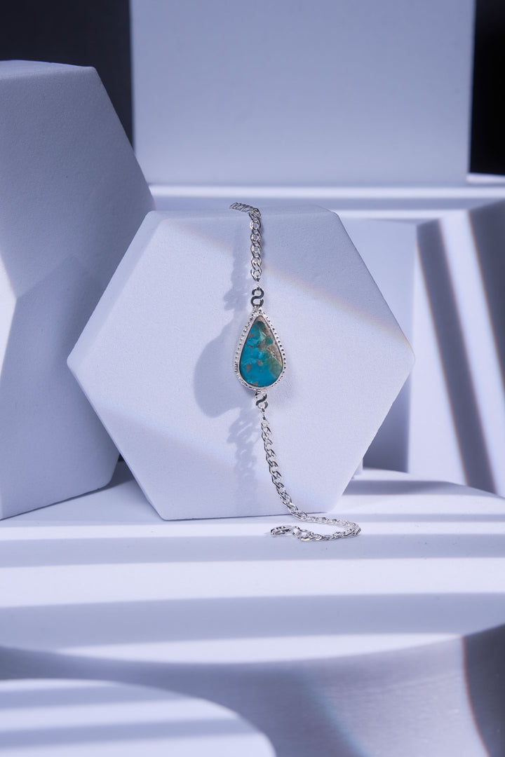 Silver bracelet with a turquoise gemstone on a white geometric background