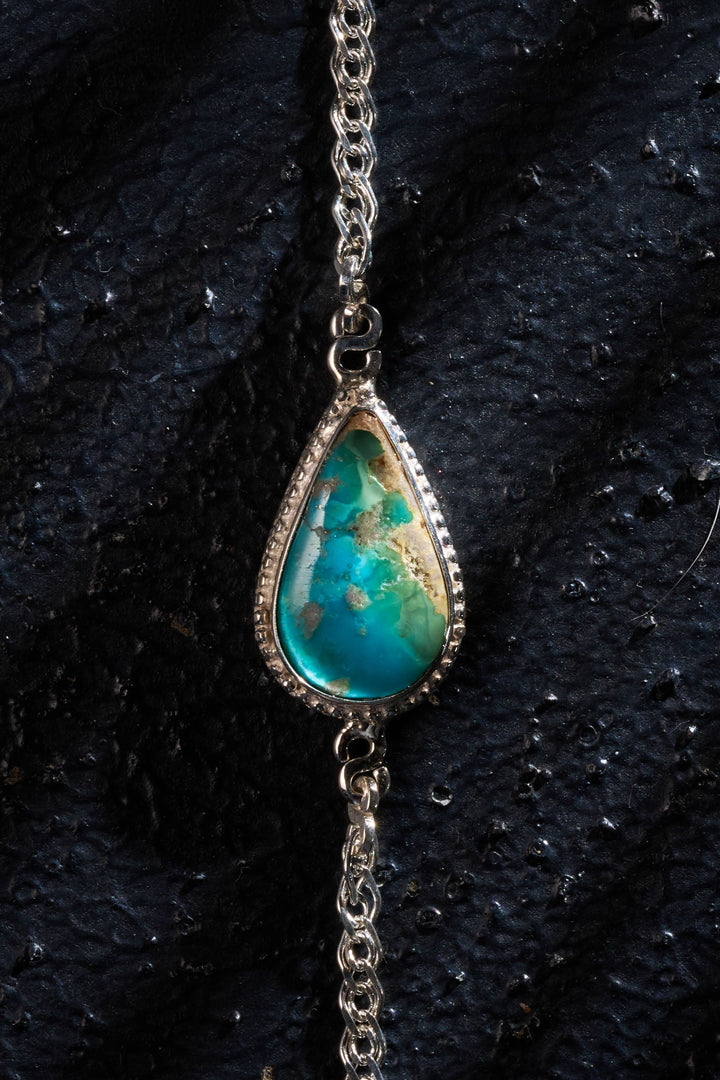 Bracelet with a teardrop-shaped turquoise stone on a dark fabric background