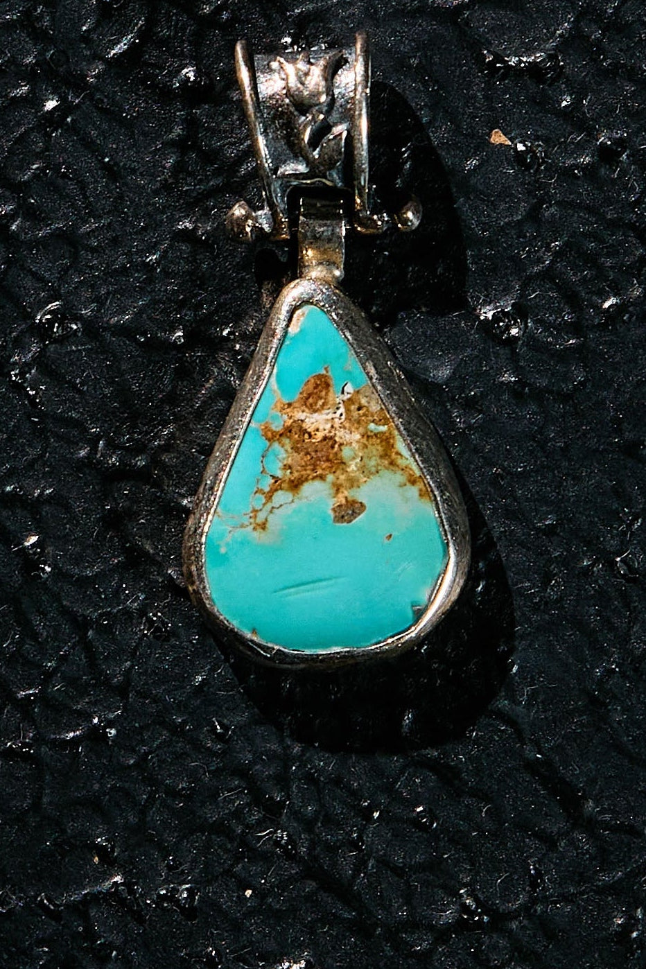Turquoise pendant with silver setting on a black textured background