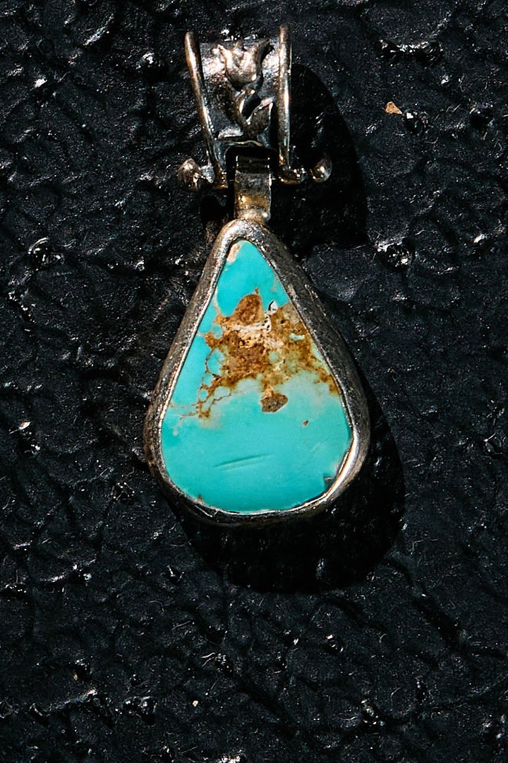 Turquoise pendant with silver setting on a black textured background