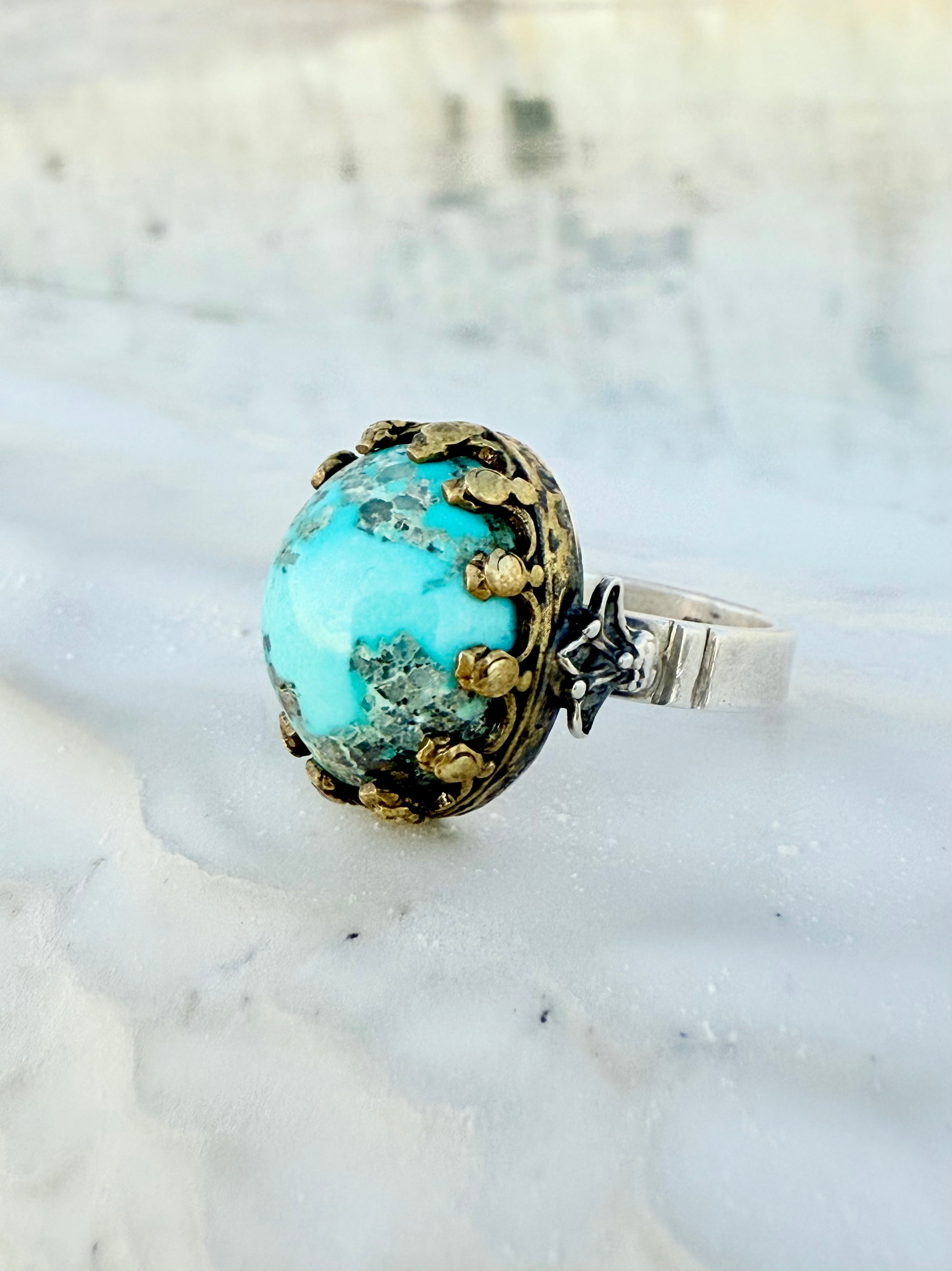 Turquoise ring with natural silver accents and one guide set in a gold-plated royal crest. 