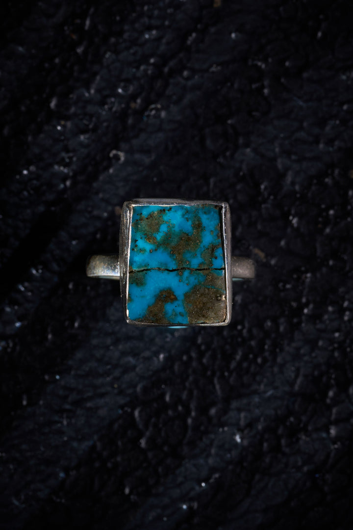 Silver ring with a square turquoise stone on a dark textured background