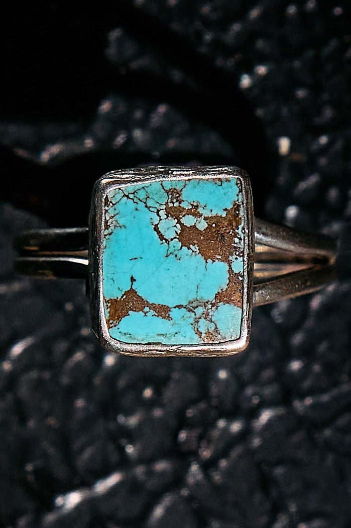 Turquoise ring with silver band on a textured black background