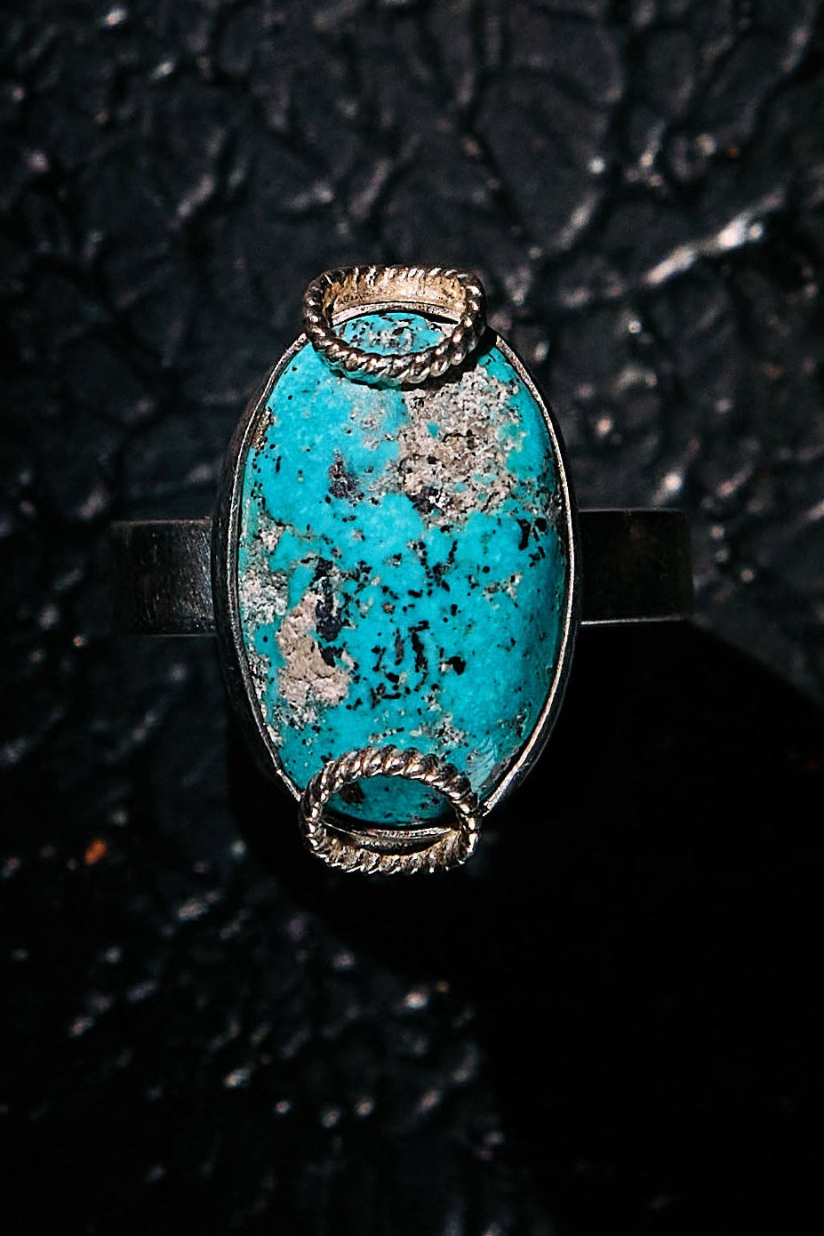 Turquoise ring with silver band on a textured black background