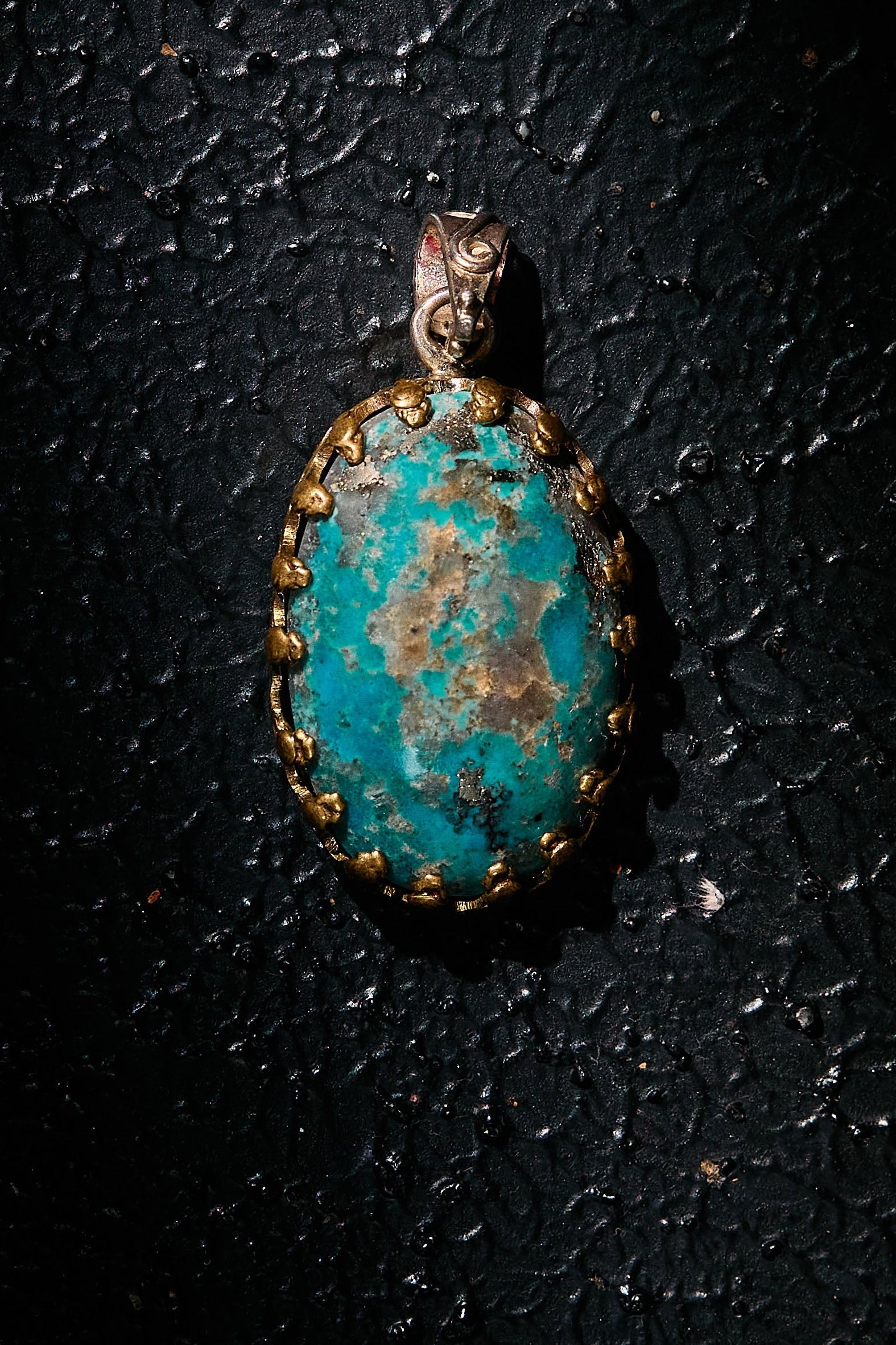 Turquoise pendant with gold accents on 925 silver on a dark textured surface
