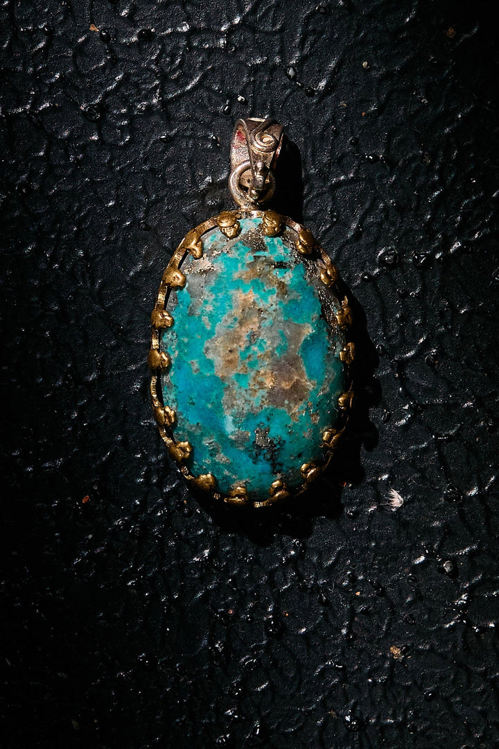 Turquoise pendant with gold accents on 925 silver on a dark textured surface