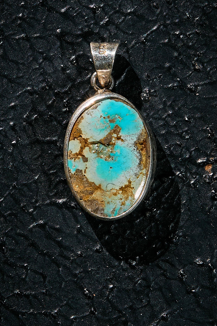 Turquoise pendant with silver setting on a black textured background