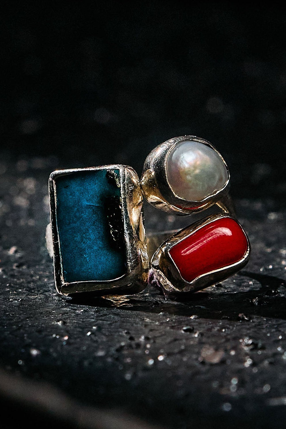 Ring with turquoise, pearl, and red stones on a dark background