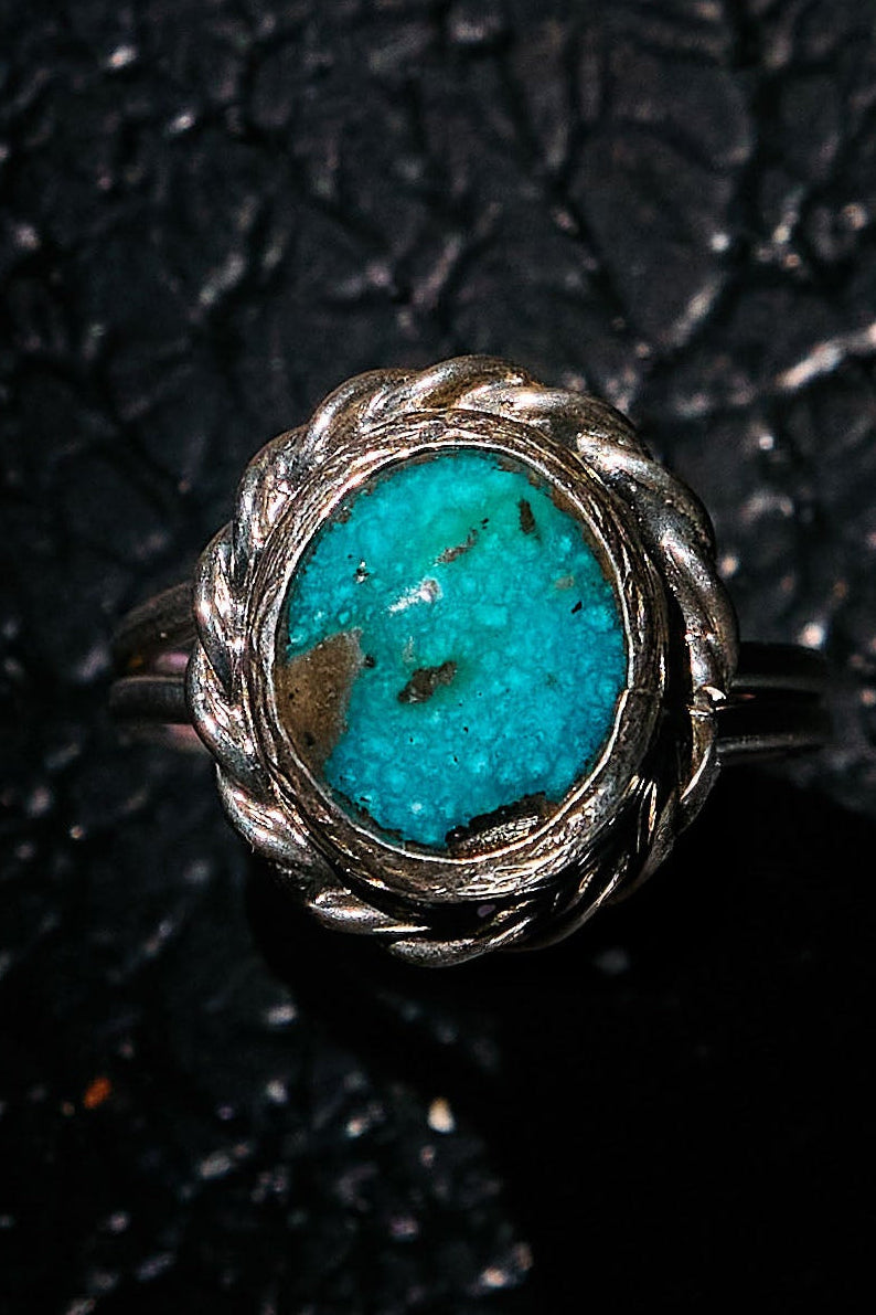 Silver ring with a turquoise stone on a textured black background