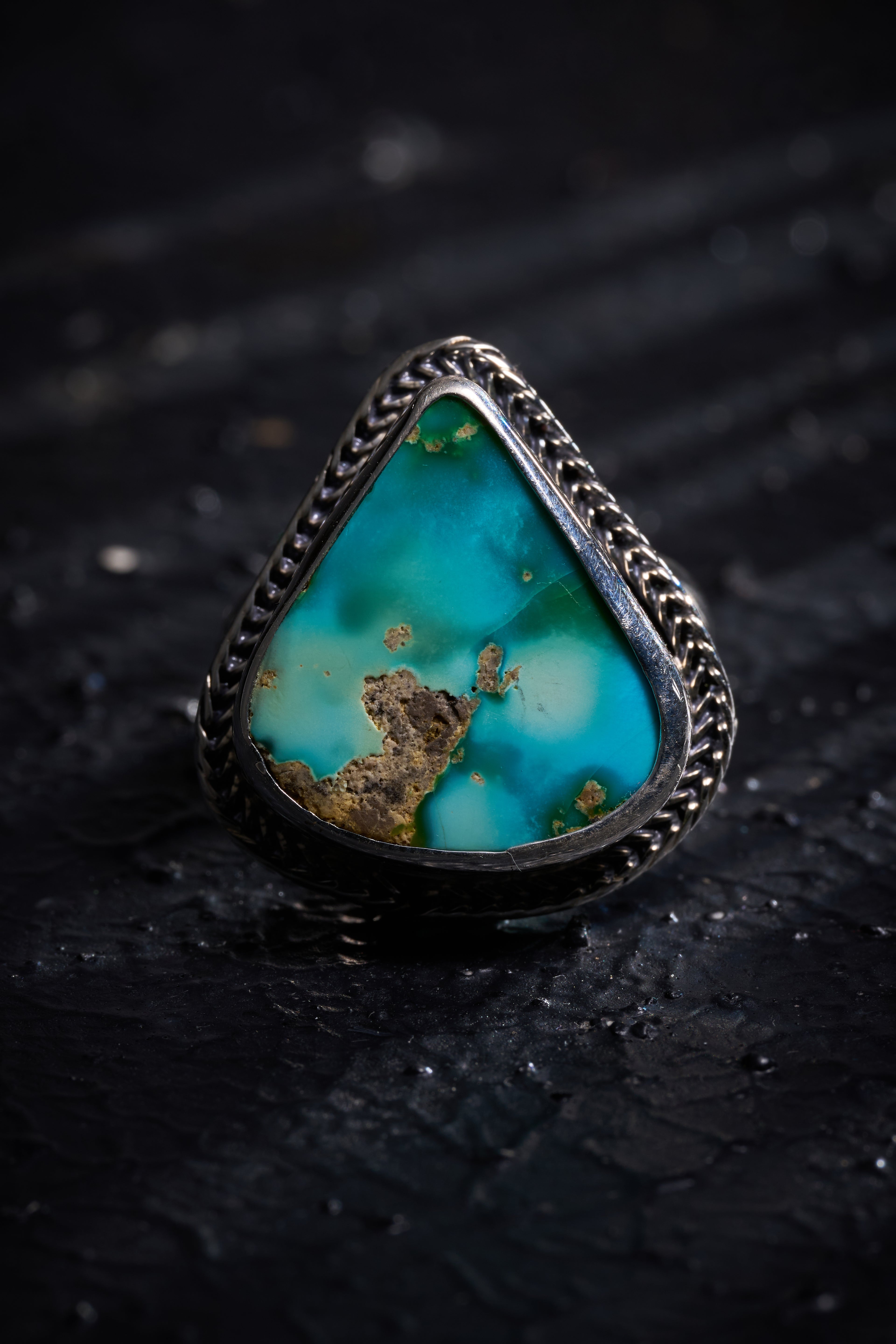 Turquoise ring with silver band on a dark textured background
