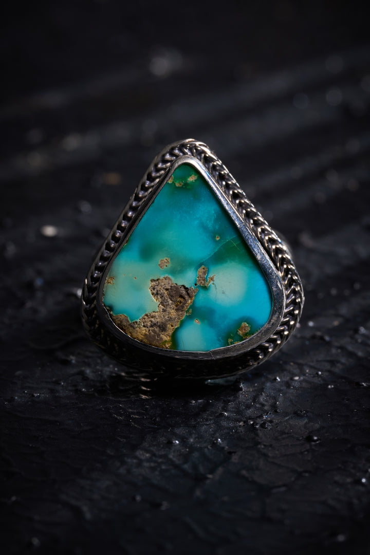 Turquoise ring with silver band on a dark textured background