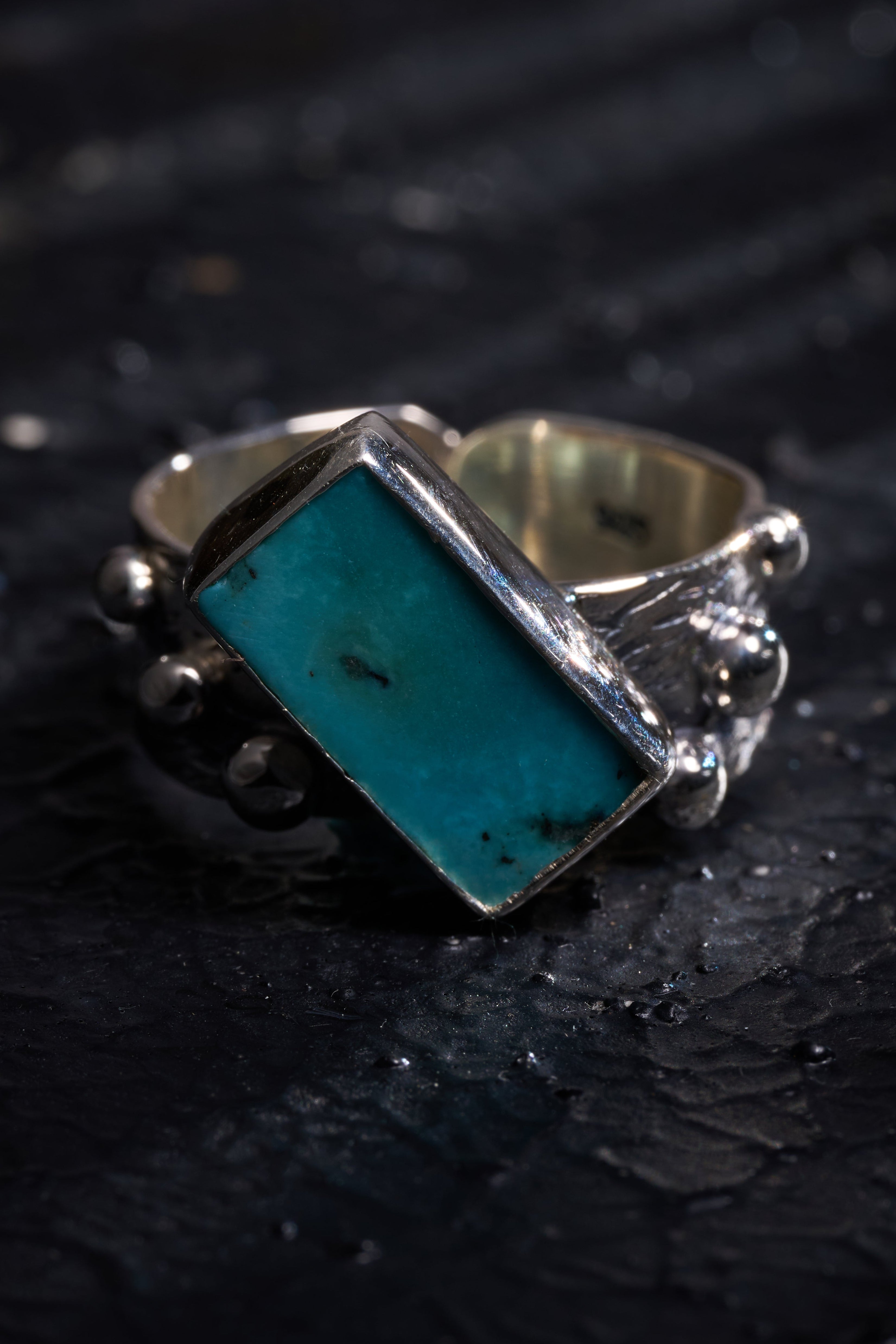 Silver ring with a turquoise stone on a dark textured surface