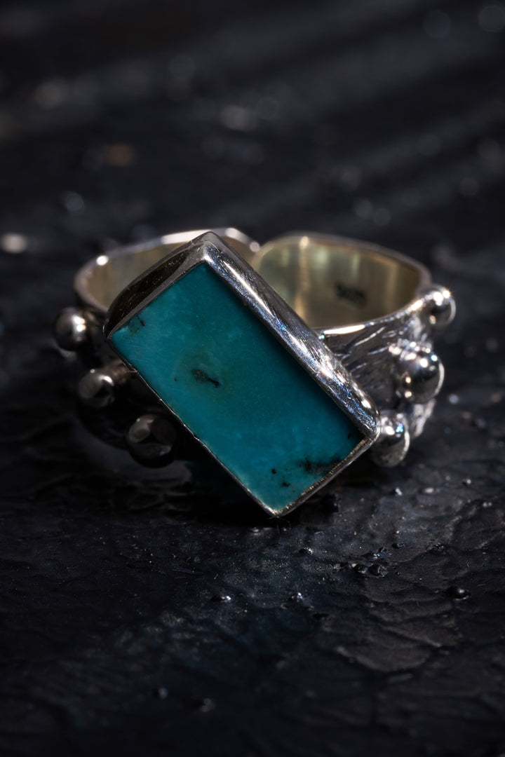 Silver ring with a turquoise stone on a dark textured surface