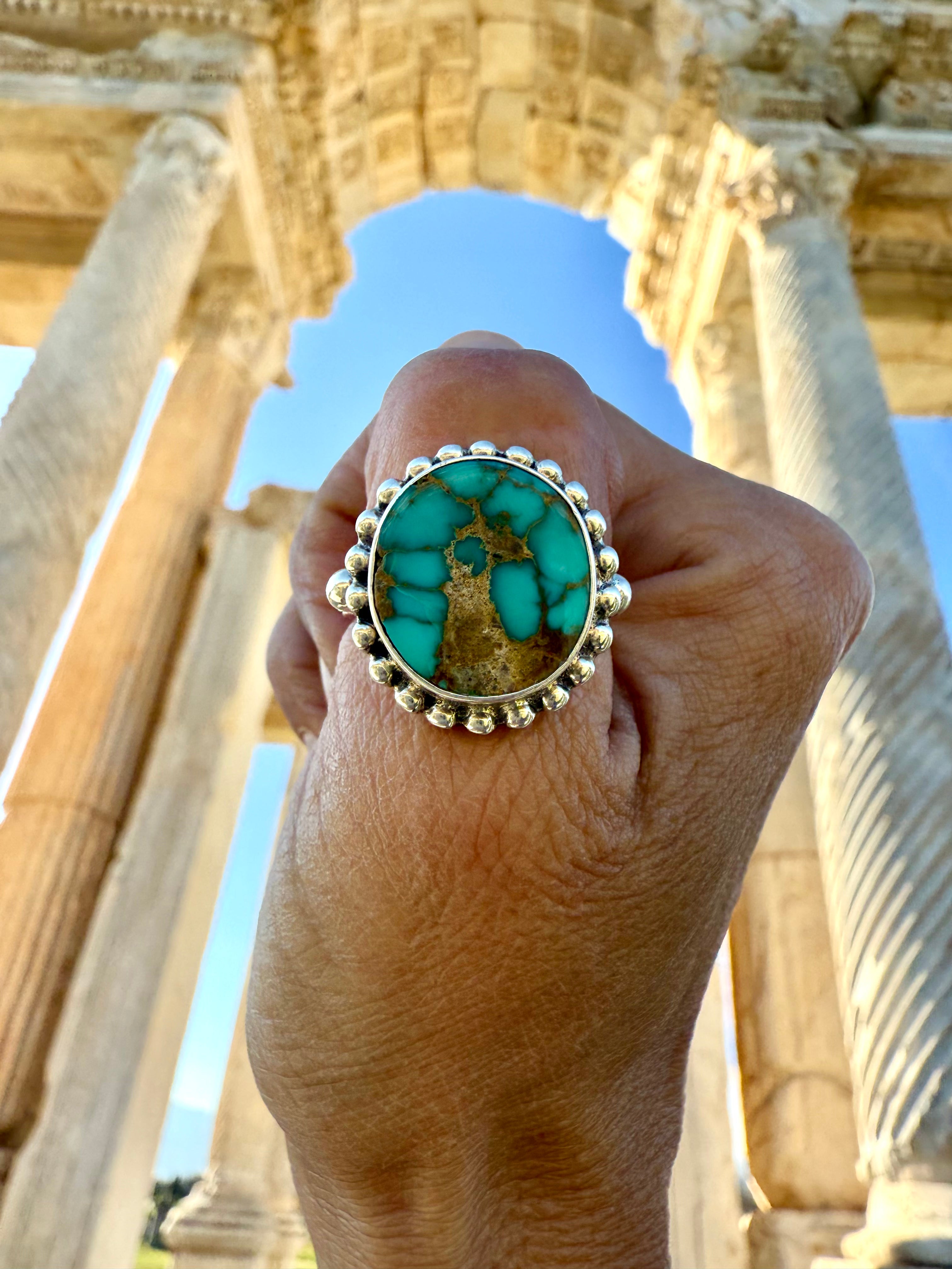 Rare natural turquoise ring with silver band held up against the Temple of Aphrodesias.