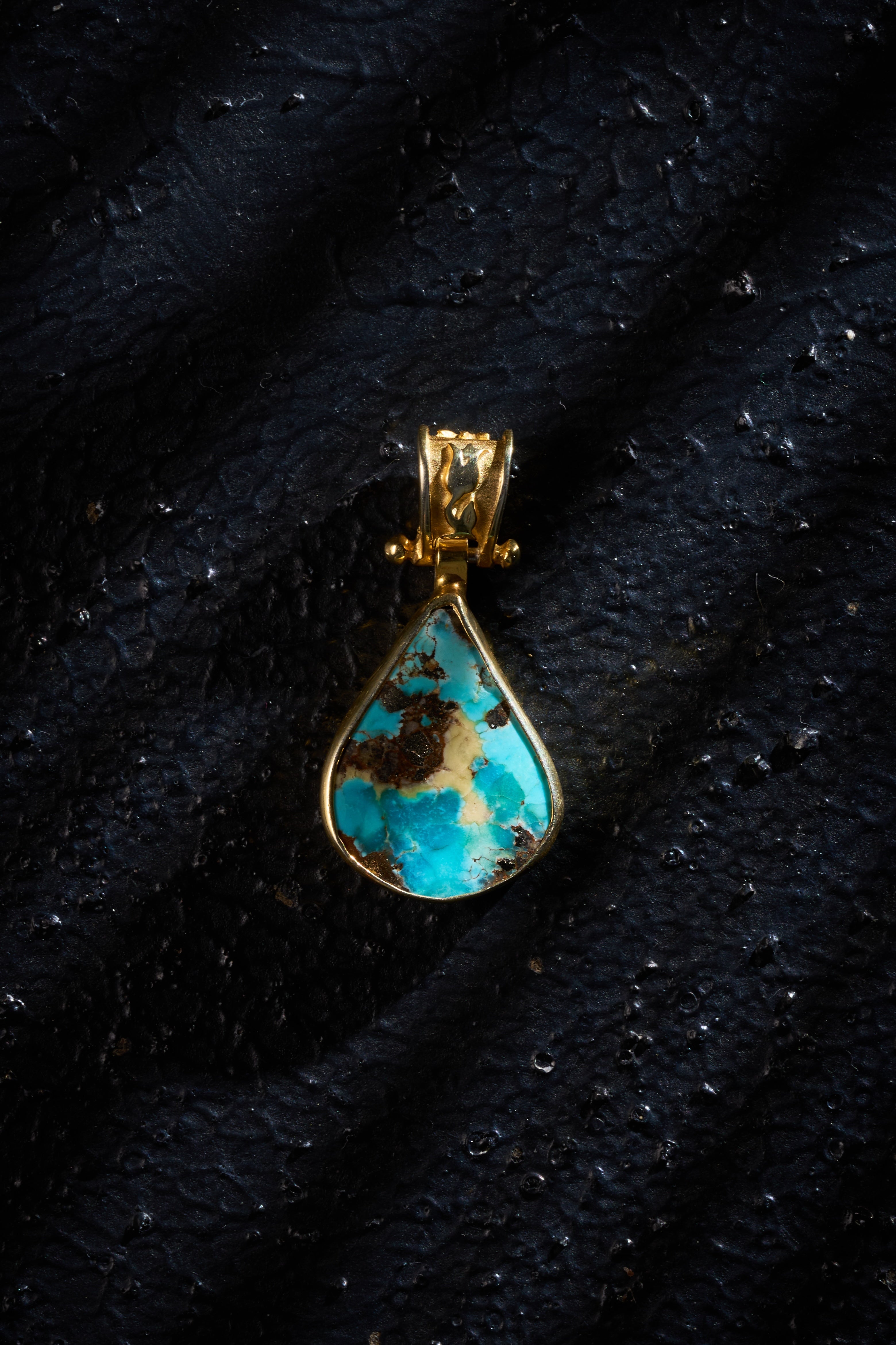 Turquoise pendant with gold plated silver setting on a black background