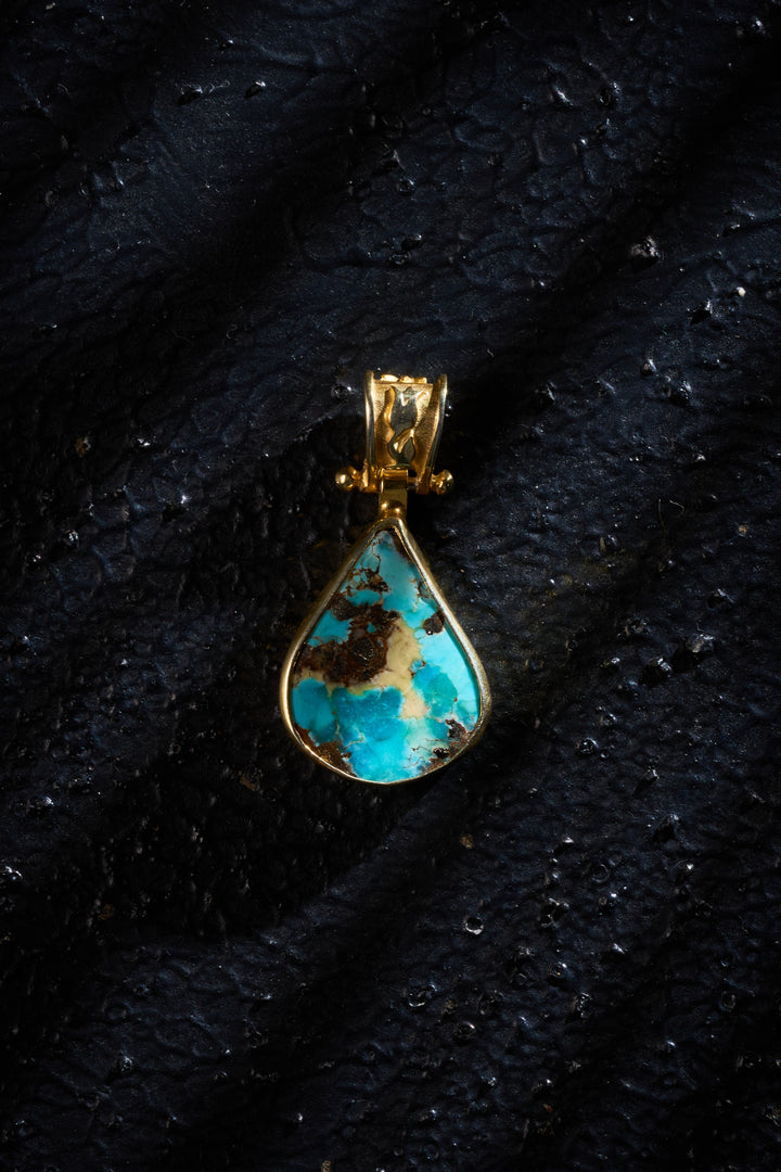 Turquoise pendant with gold plated silver setting on a black background