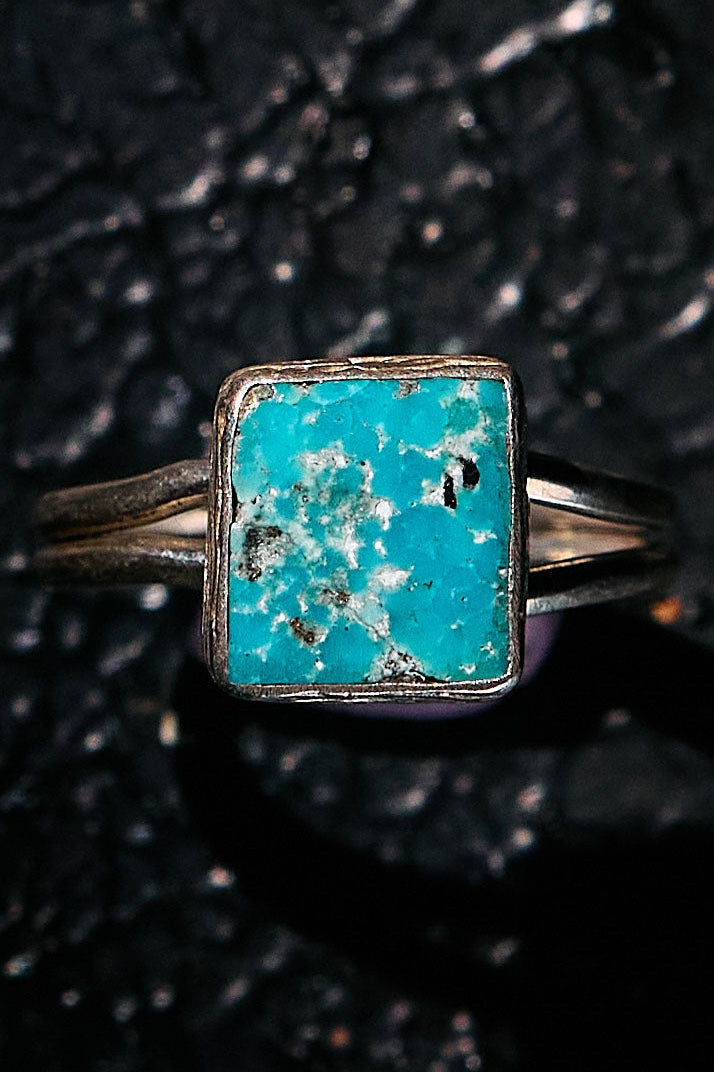 Turquoise ring with silver band on a textured black background
