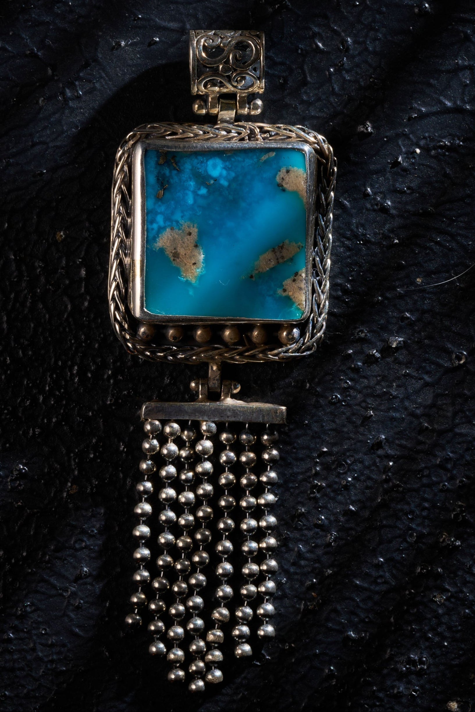 Silver pendant with a turquoise on a textured black surface