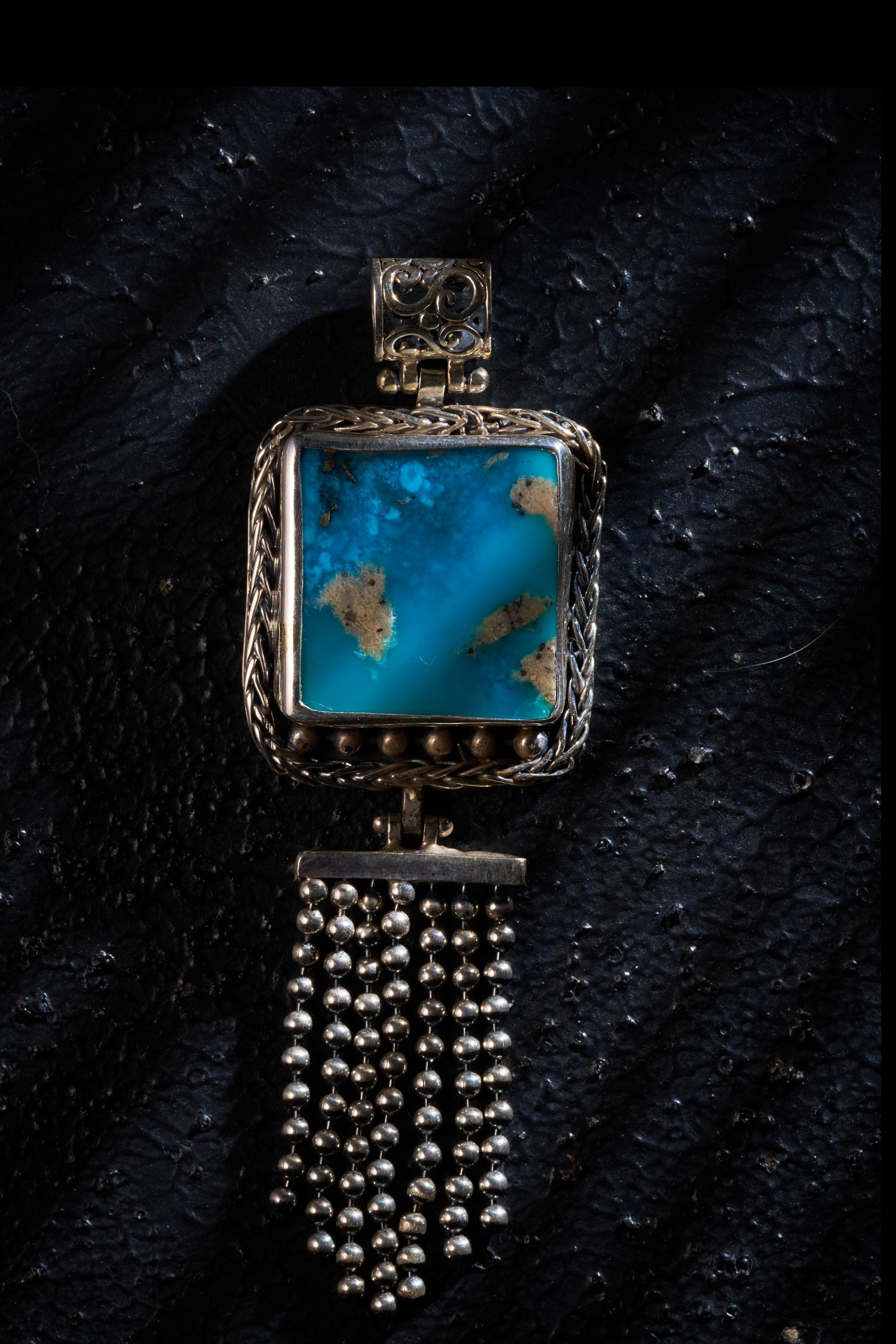 Silver pendant with a turquoise on a textured black surface