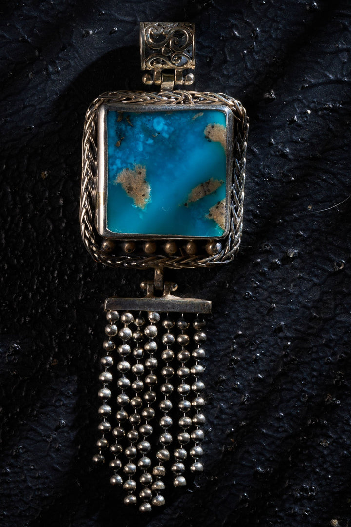 Silver pendant with a turquoise on a textured black surface