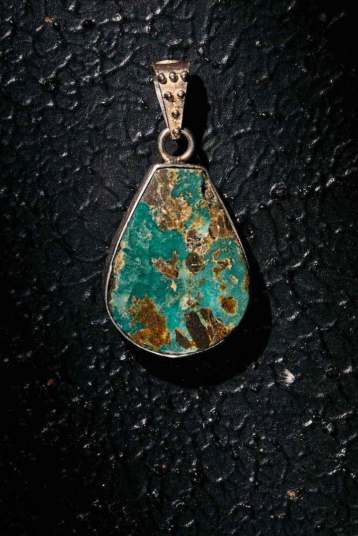 Teardrop-shaped turquoise pendant on a dark textured background