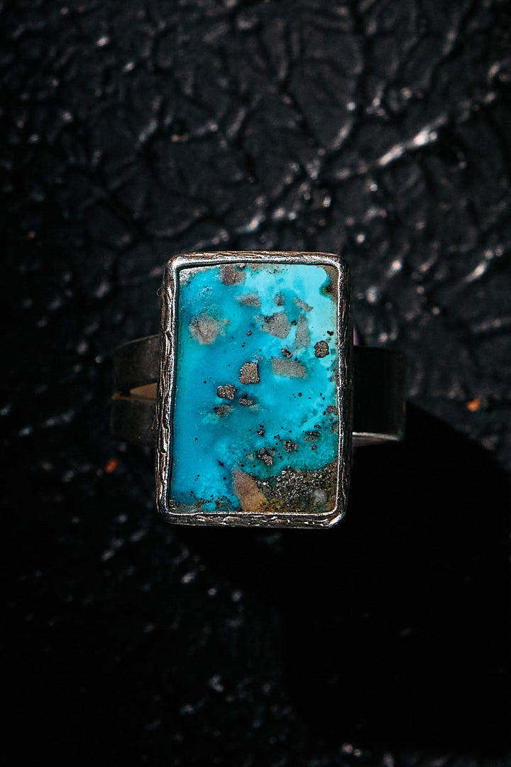 Turquoise stone ring with silver frame on a textured black background