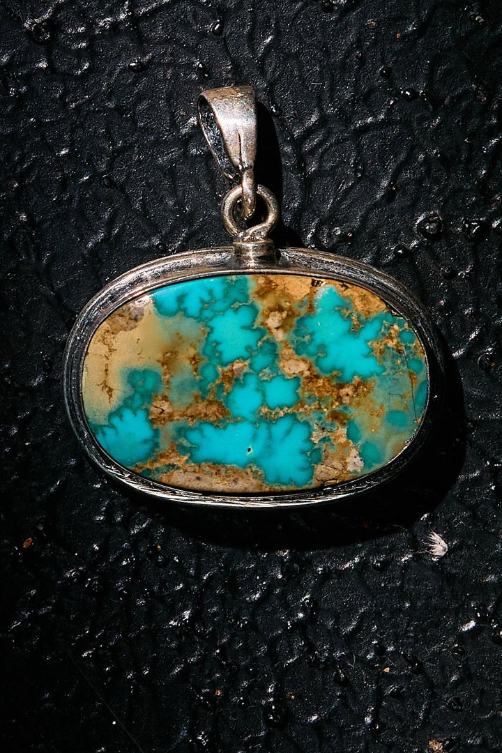 Turquoise pendant with silver setting on a black textured background