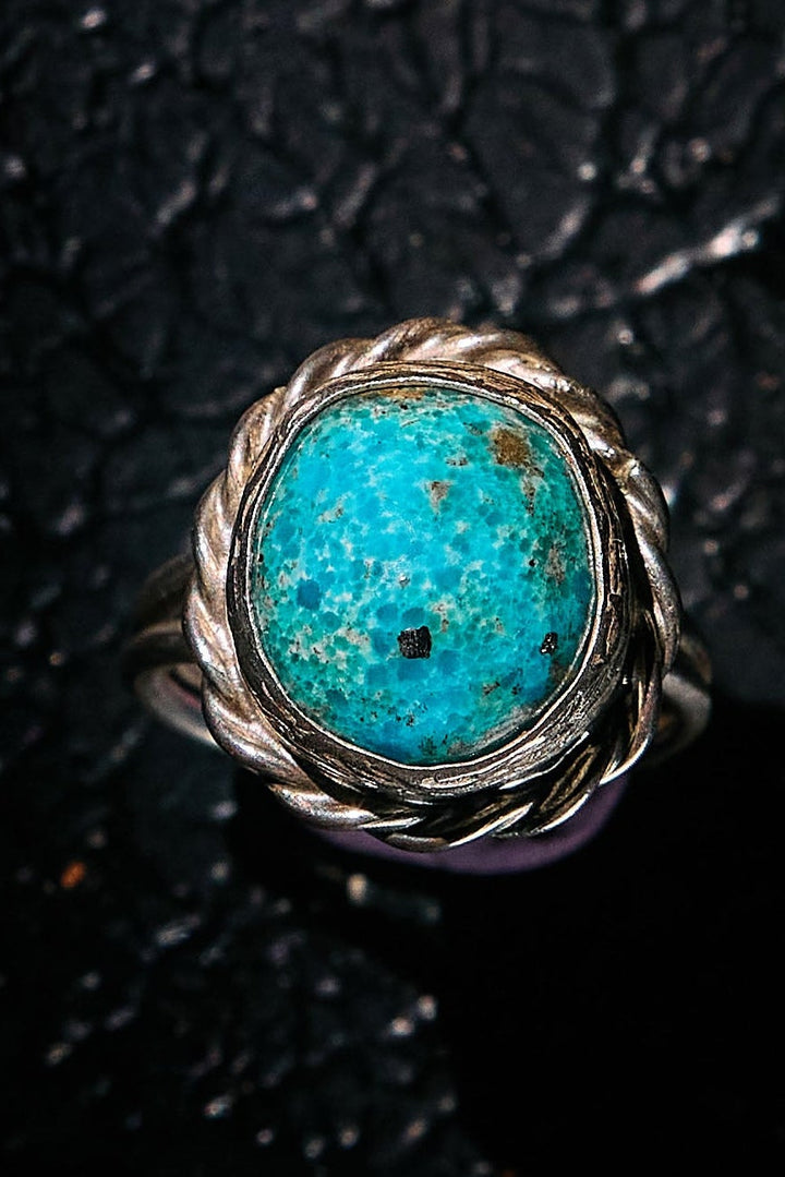 Turquoise ring with silver band on a textured black background