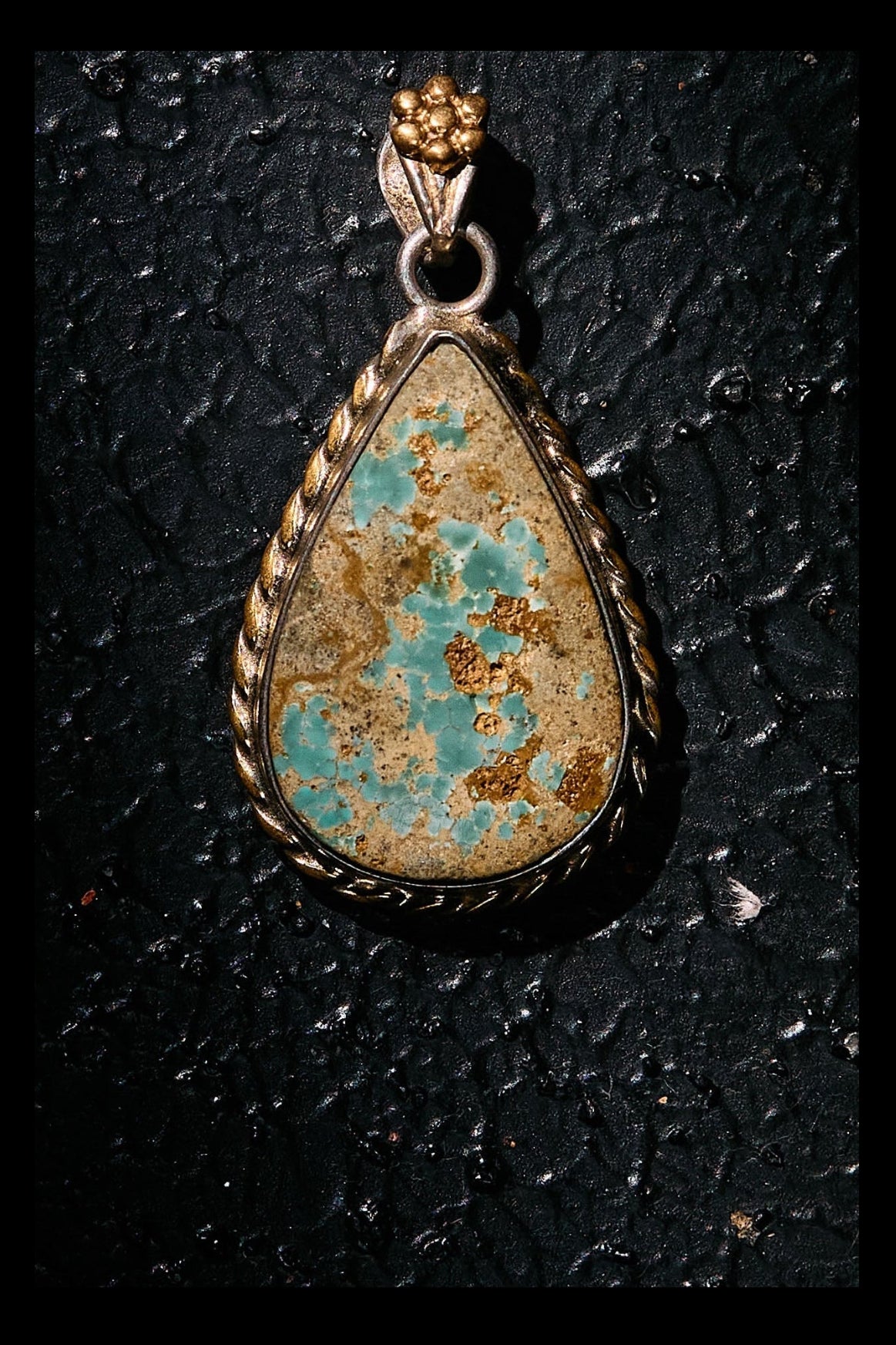 Teardrop-shaped turquoise pendant on a black textured background