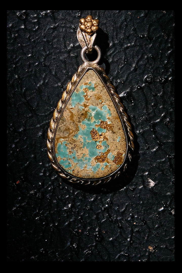 Teardrop-shaped turquoise pendant on a black textured background